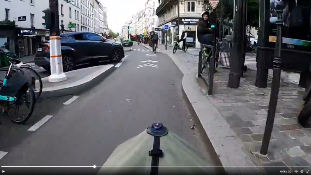 Capture d'écran d'une vidéo de dashcam venant d'un cycliste. Le cycliste est sur une piste cyclable séparée du trafic par un stationnement vélo. À sa gauche, une voie motorisée allant dans le même sens.

Le cycliste a sa voie libre et un feu vert pour le carrefour qui s'annonce.

Sur sa gauche, à quelques mètres, un automobiliste est situé dans l'espace de stockage pour tourner à droite (donc couper le trajet du cycliste) mais n'a pas encore dépassé la ligne de séparation.